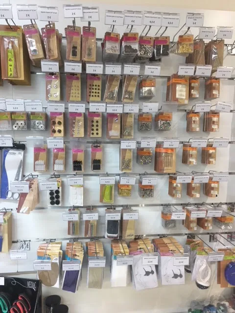 Boutons, pressions, œillets et petits accessoires de couture présentés sur un mur de la mercerie